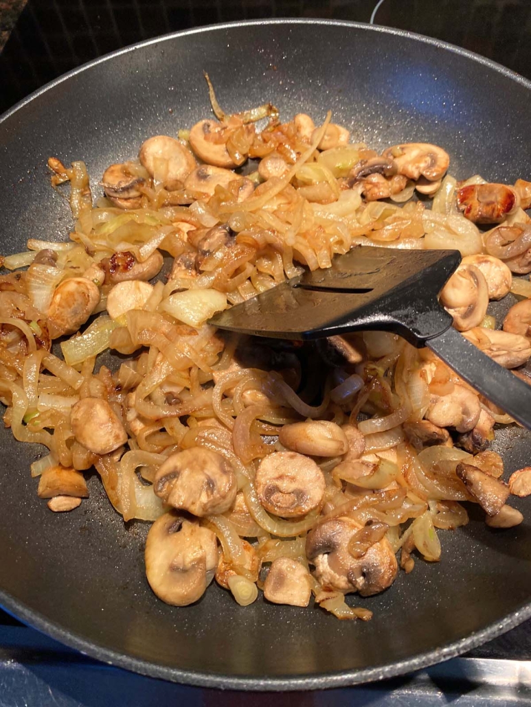 using spatula to mix mushrooms and onions with seasoning