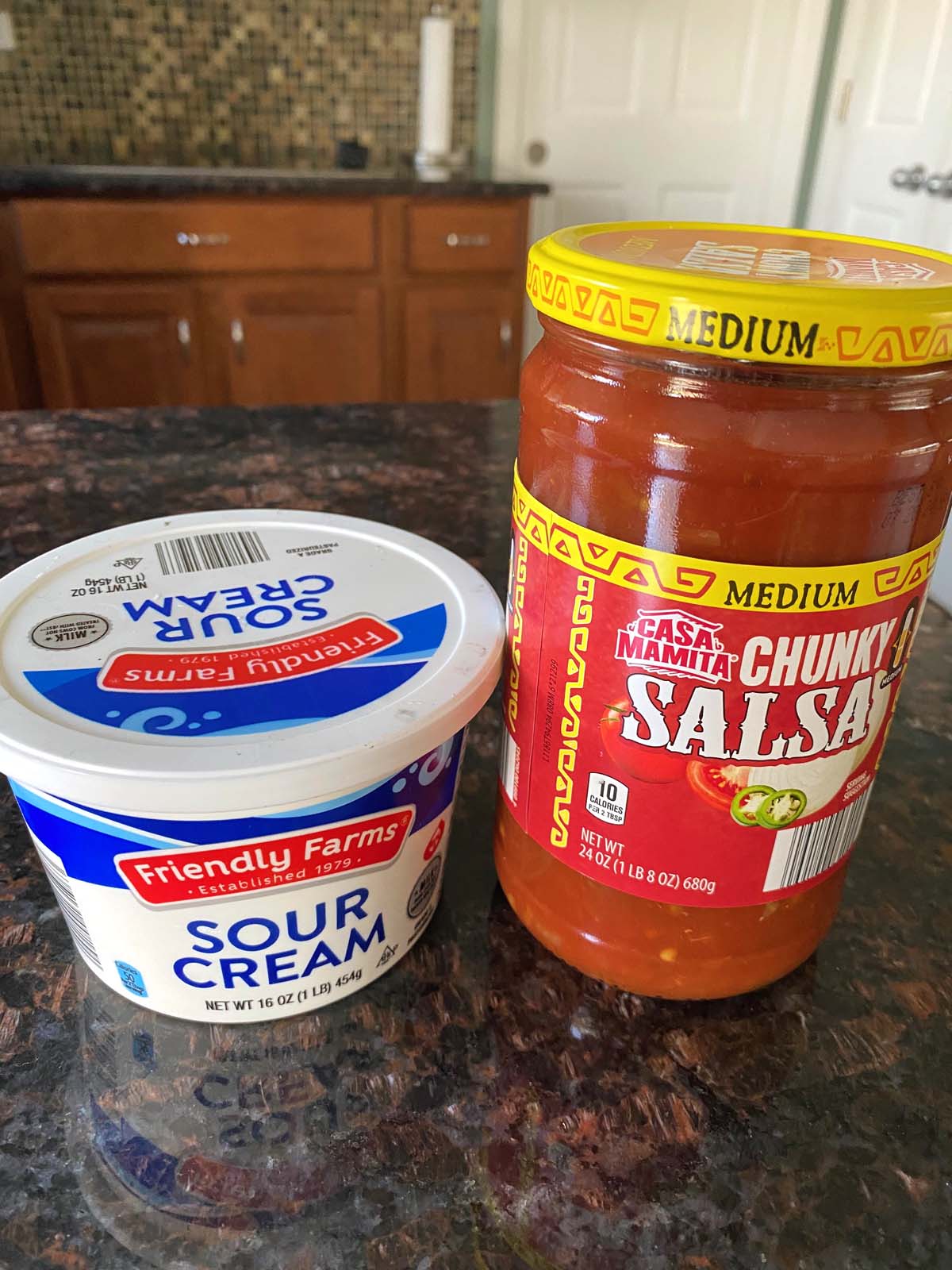 A container of sour cream and jar of salsa.