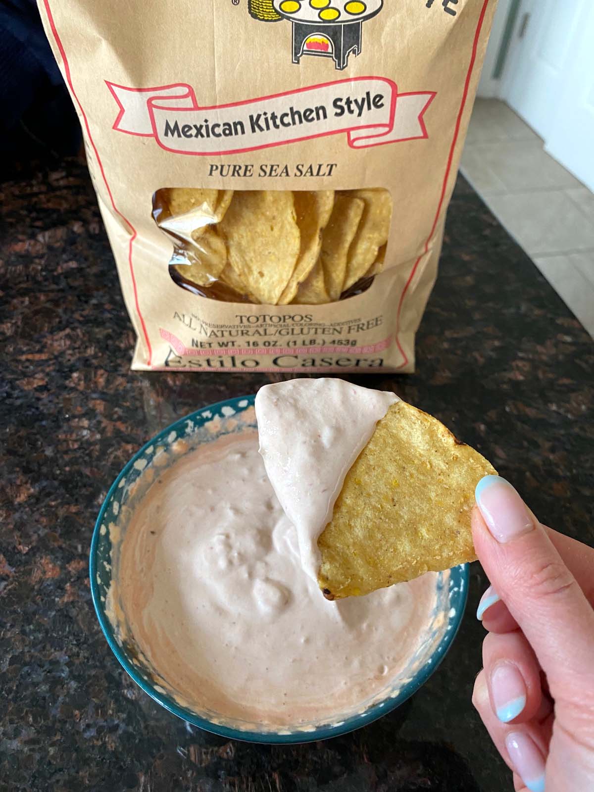 Bowl of sour cream and salsa dip with a bag of tortilla chips next to it. 