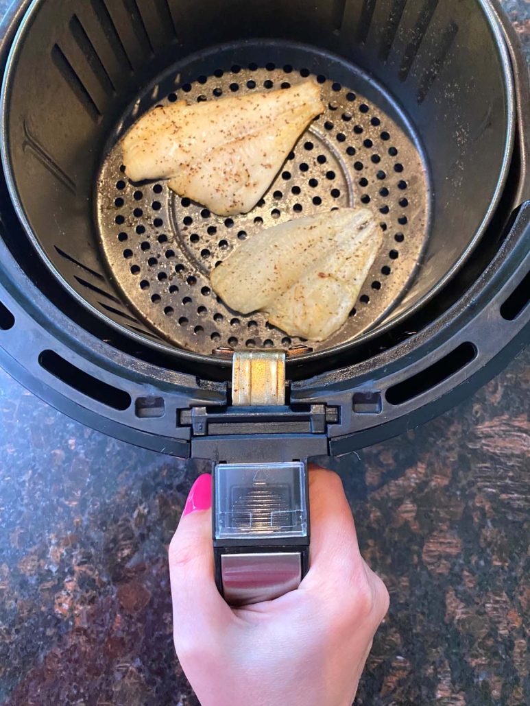 hand holding air fryer basket with flounder fish inside