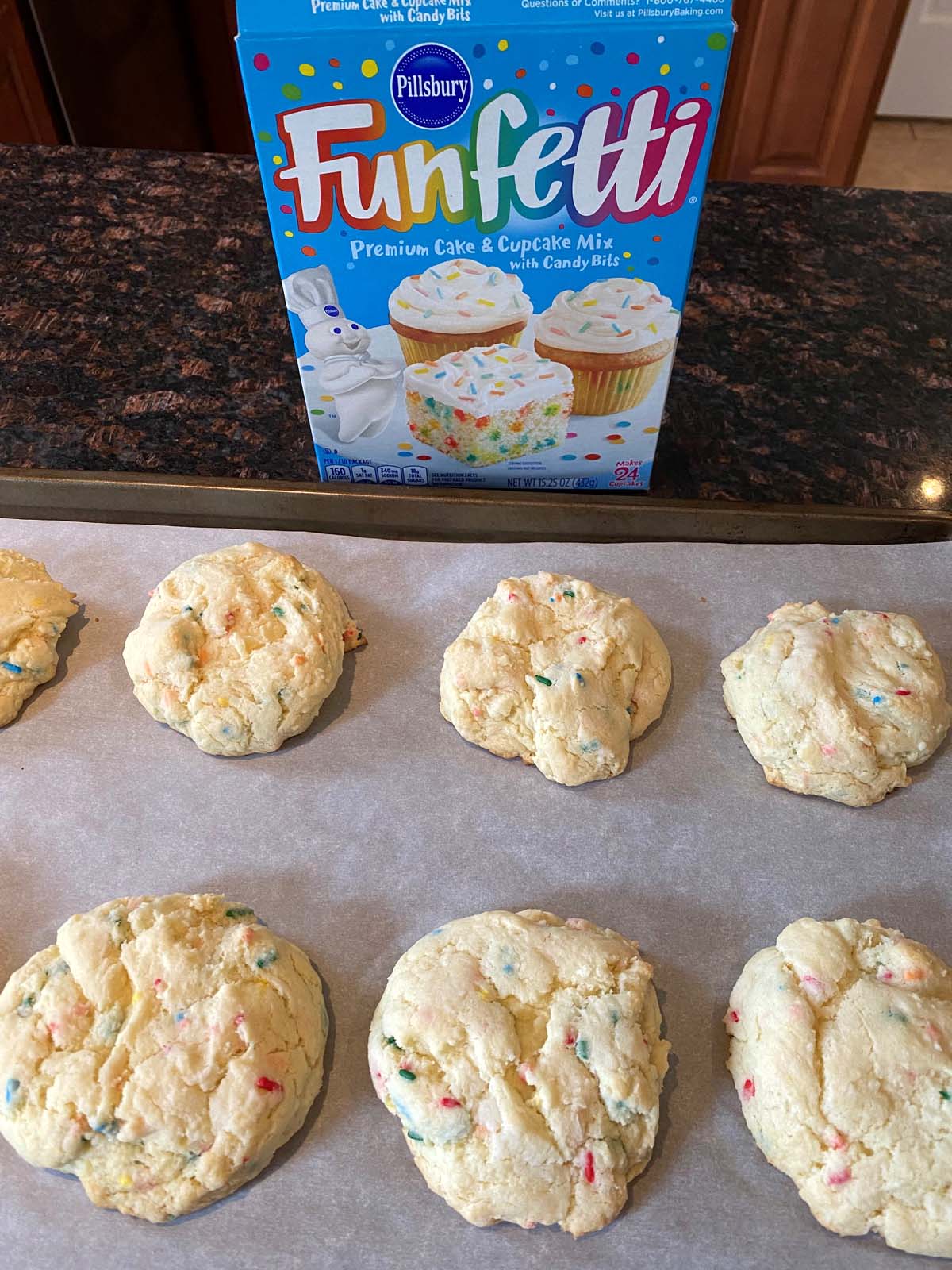 Funfetti cake mix cookies on a sheet pan and a box of funfetti cake mix. 