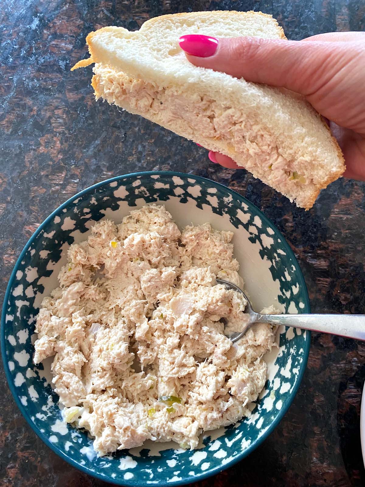 Shredded chicken salad in a bowl and half a sandwhich.