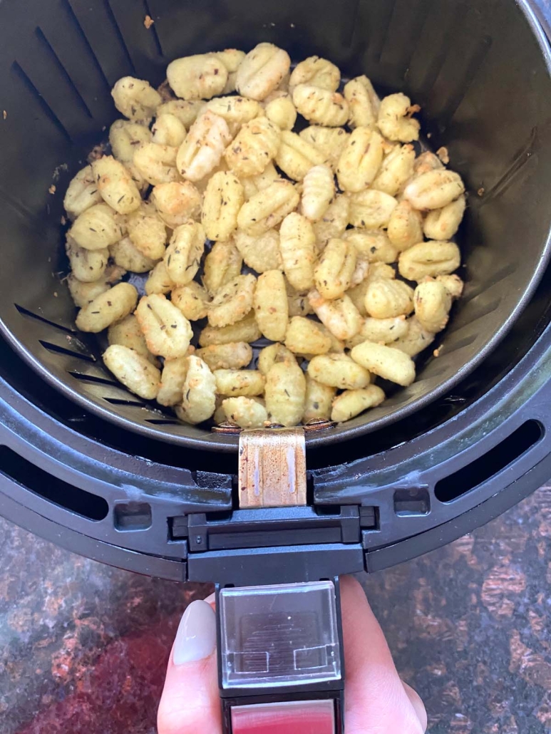 hand holding air fryer basket with cooked gnocchi inside