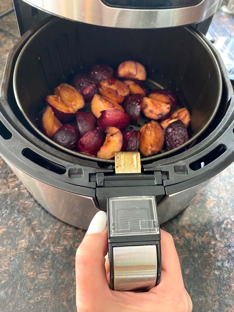 hand holding air fryer basket with roasted plums inside