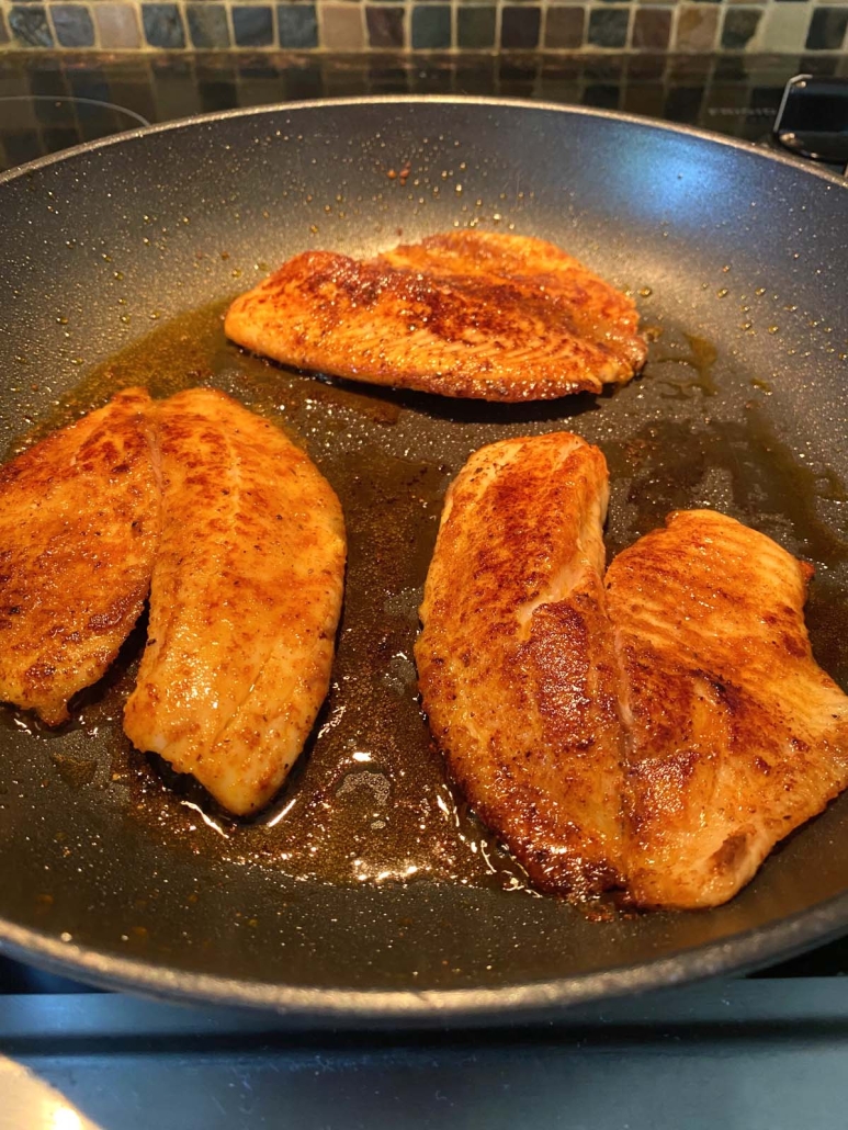 seasoned tilapia cooking in pan