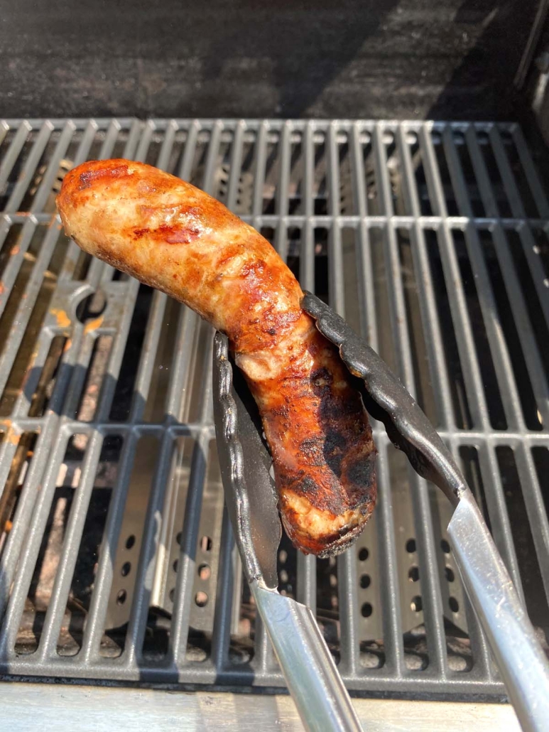 tongs holding cooked Italian sausage