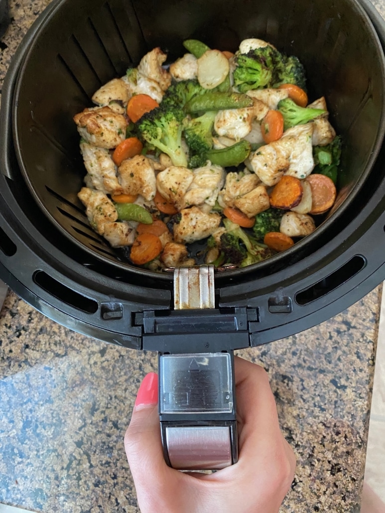 hand holding air fryer basket with chicken and vegetables