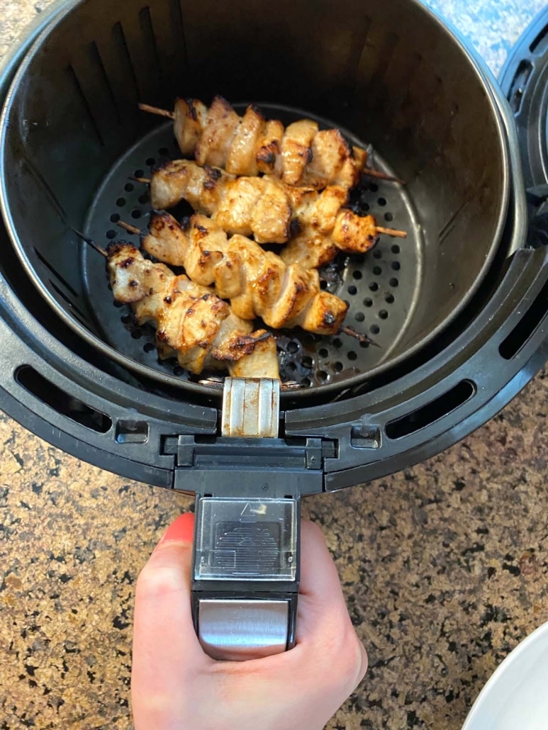 hand holding air fryer basket with chicken kabobs inside