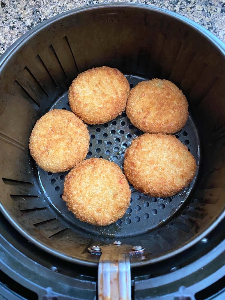 air fryer basket with frozen lobster cakes inside