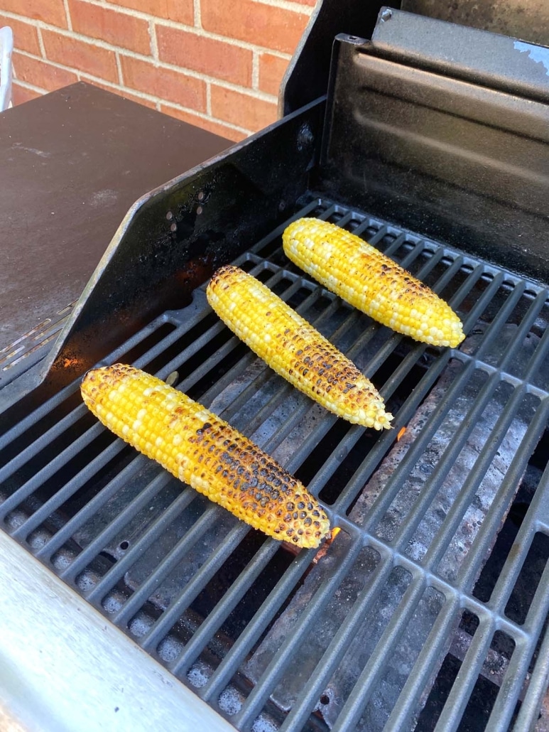 grill opened to show cooking corn cobs