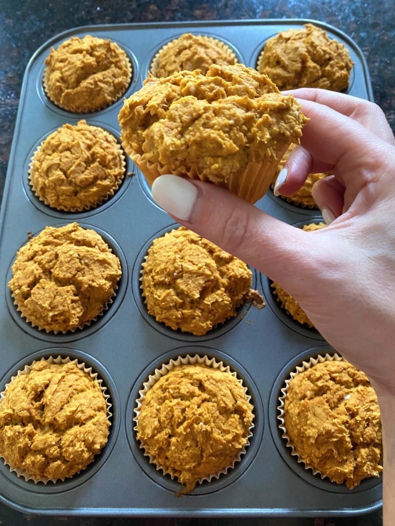 hand holding pumpkin muffin in front of baking tray