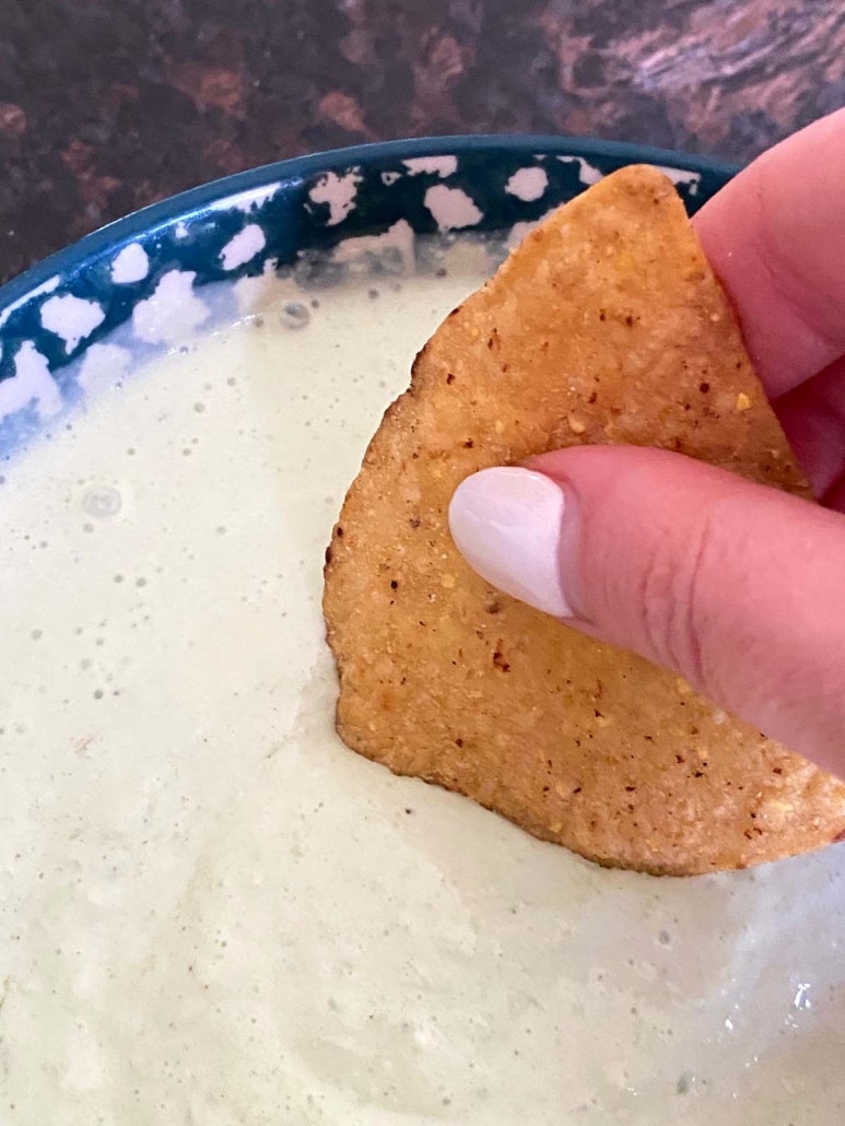 hand dipping a chip into green onion dip made with sour cream 