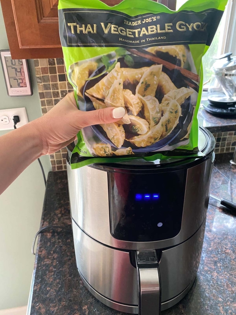 hand holding package of Trader Joe's frozen gyoza in front of an air fryer