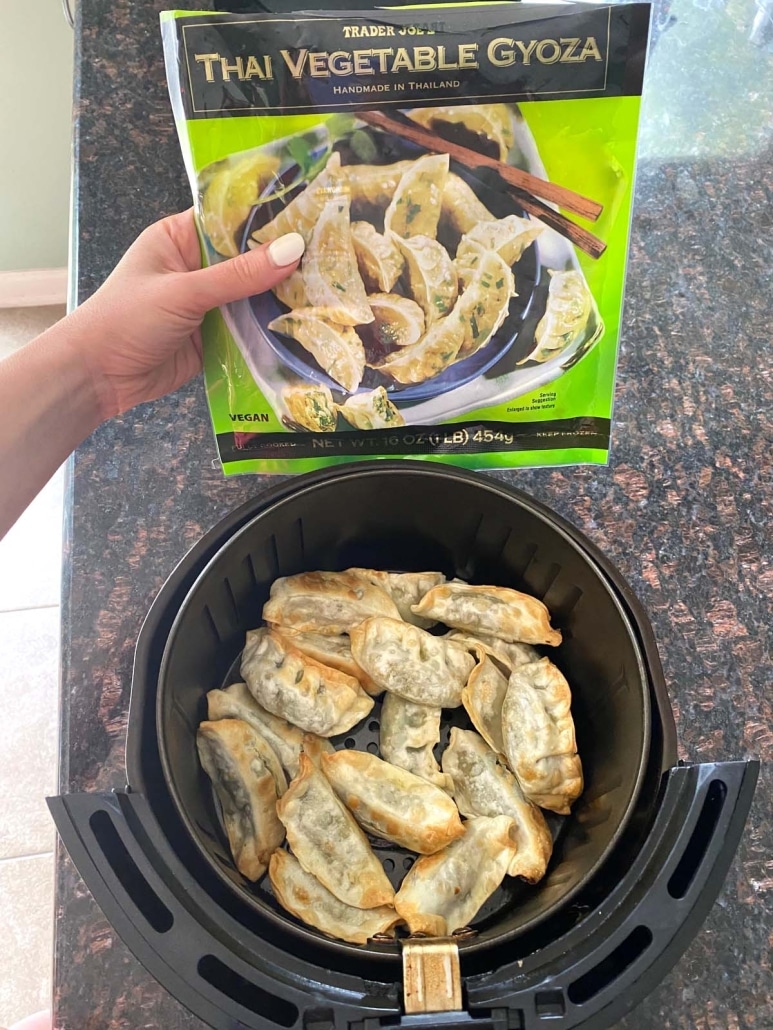 hand holding package of Trader Joe's frozen gyoza next to a batch of gyoza in an air fryer basket