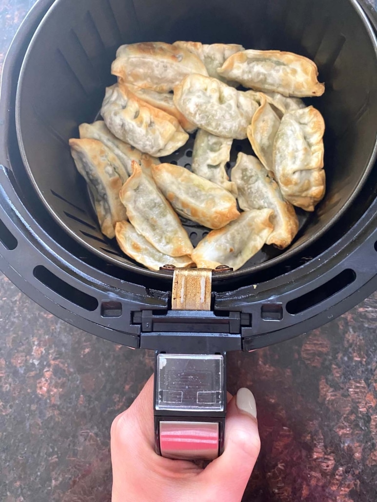 hand holding air fryer basket with Trader Joe's gyoza inside