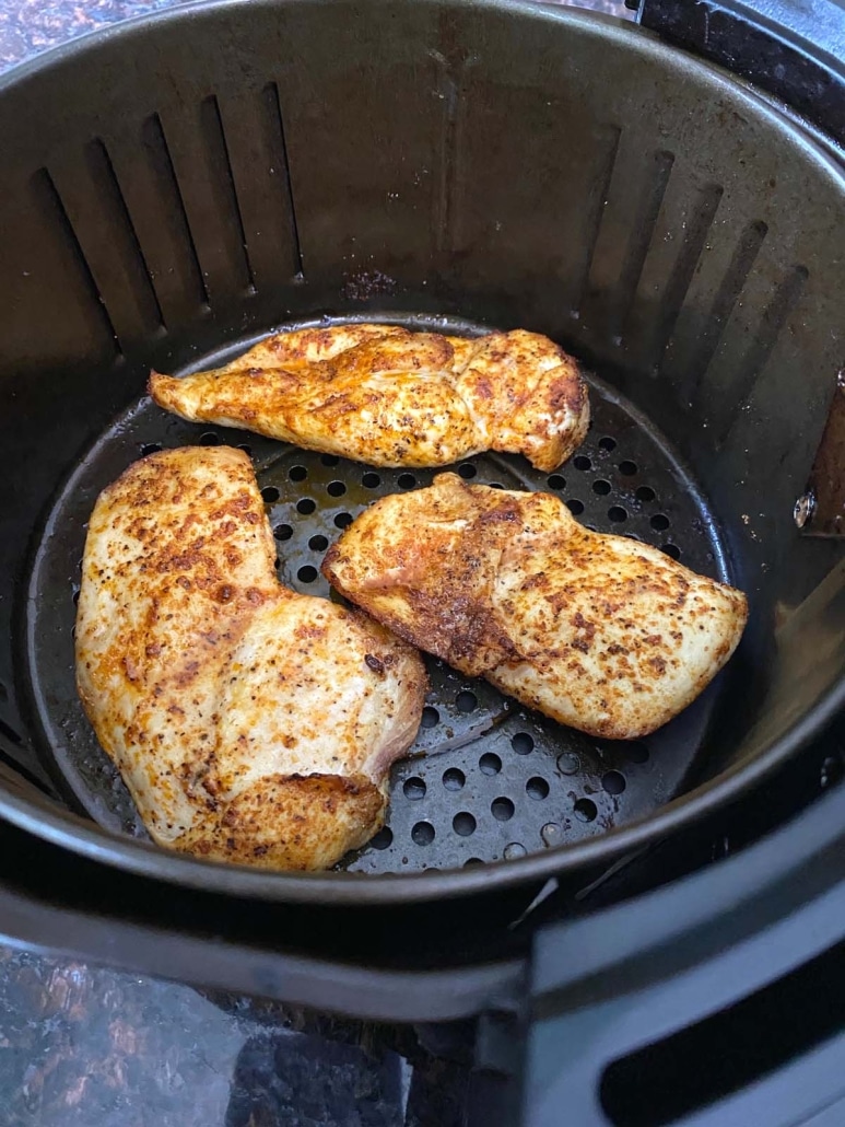 air fryer basket with seasoned chicken breasts inside