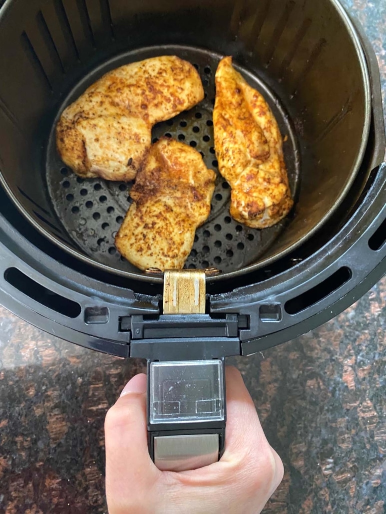 hand holding air fryer basket with Thin Sliced Chicken Breasts inside