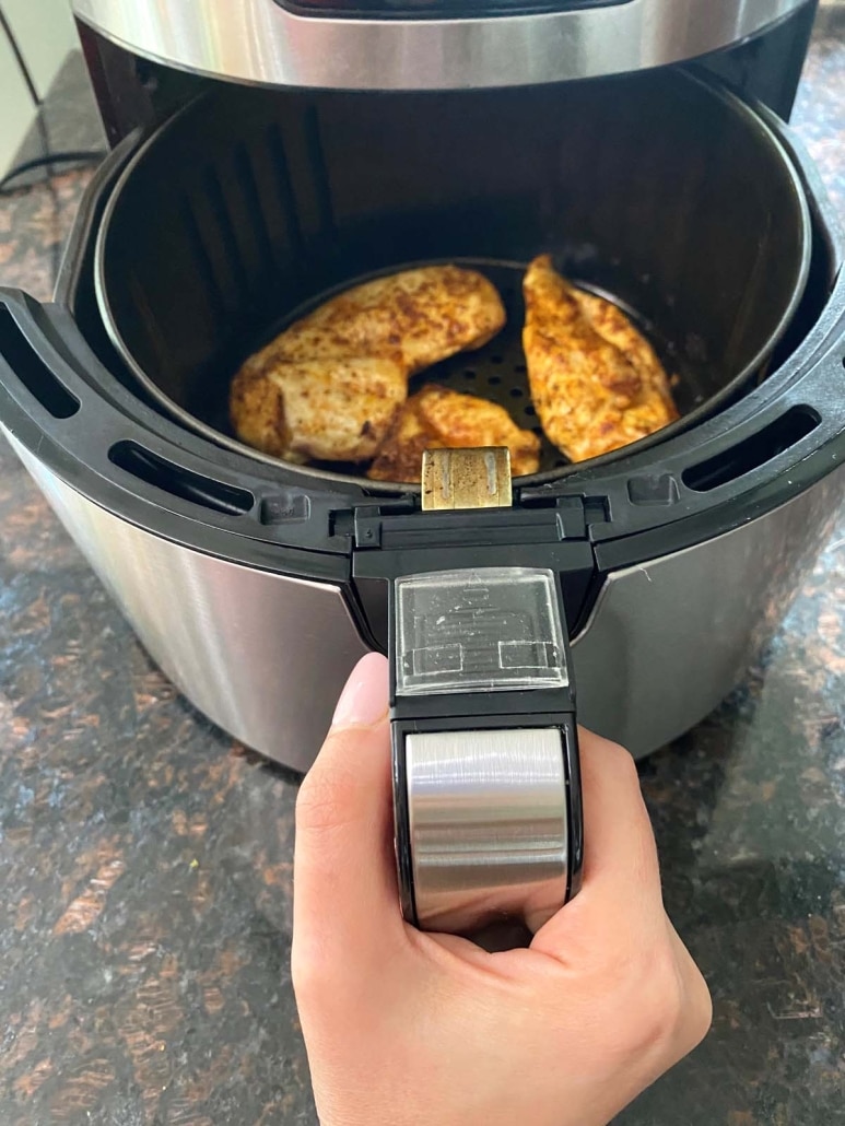 hand opening air fryer to show tender, juicy, thin sliced chicken breasts inside