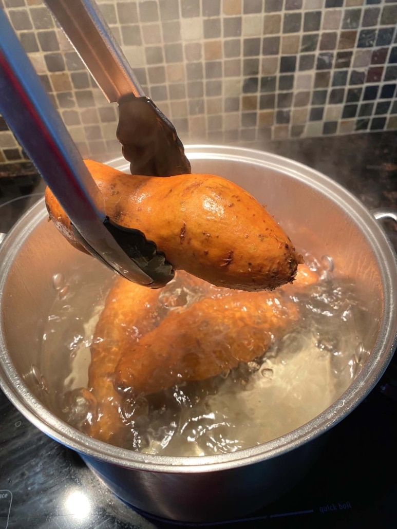 tongs pulling a cooked sweet potato out of the water