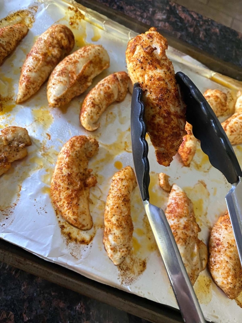 tong holding a seasoned and broiled chicken tender