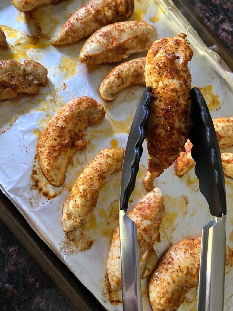 tongs holding a broiled chicken tender