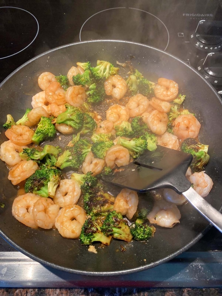 spatula mixing shrimp and broccoli in stir fry sauce