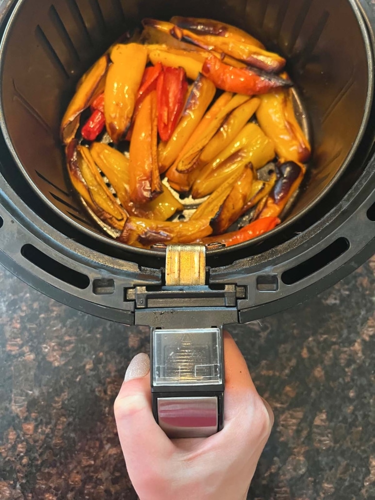 hand holding air fryer basket with mini peppers inside