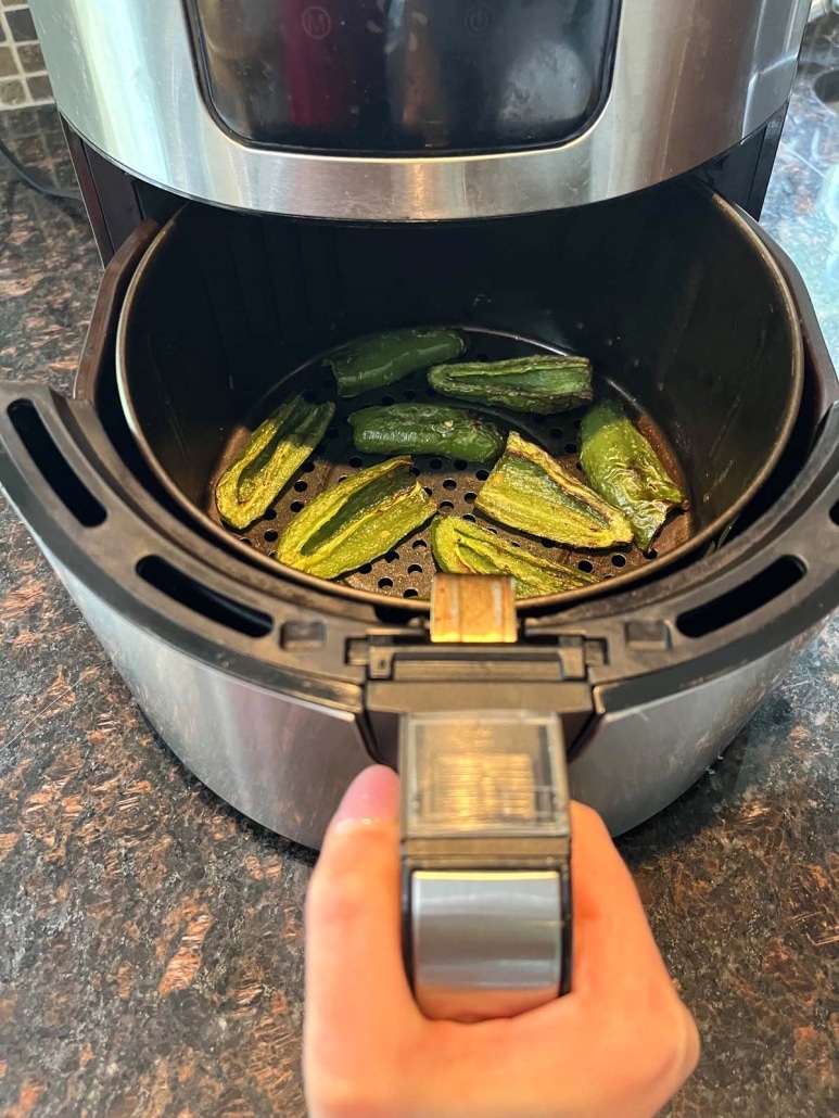 hand opening air fryer to show jalapeños cooking inside