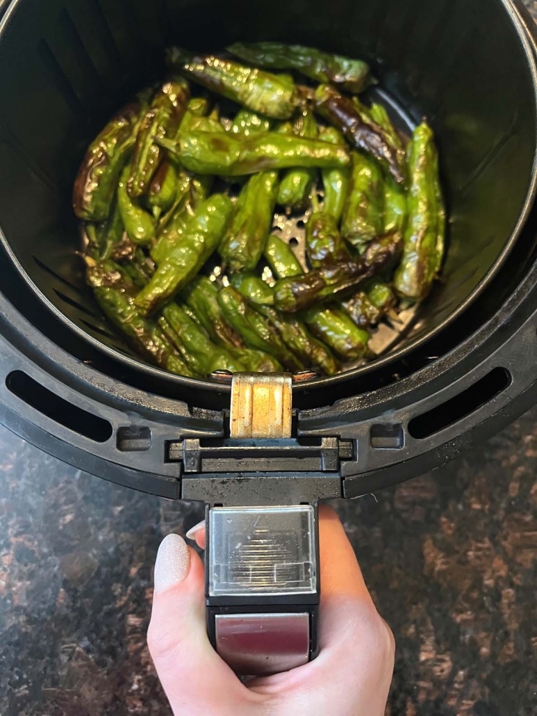 hand holding air fryer basket with cooked shishito peppers inside