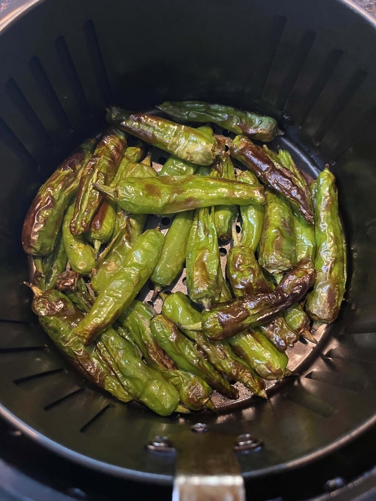 air fryer basket with shishito peppers inside