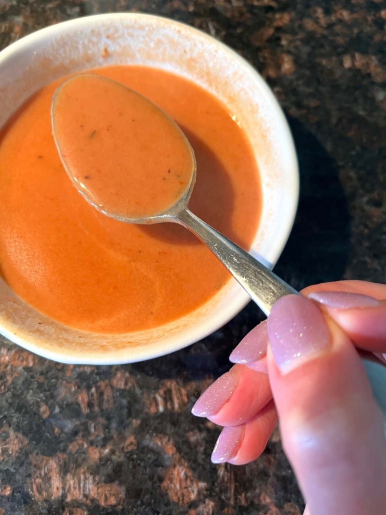 hand scooping up Tomato Soup with a spoon