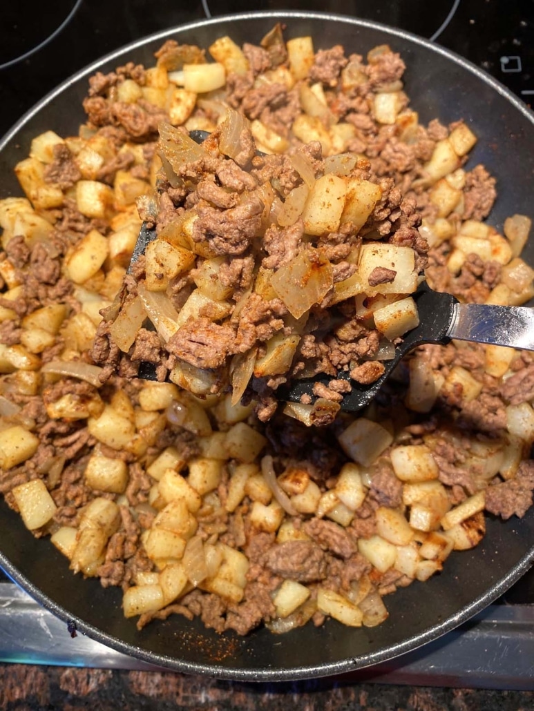 spatula mixing up cooked ground beef and potatoes