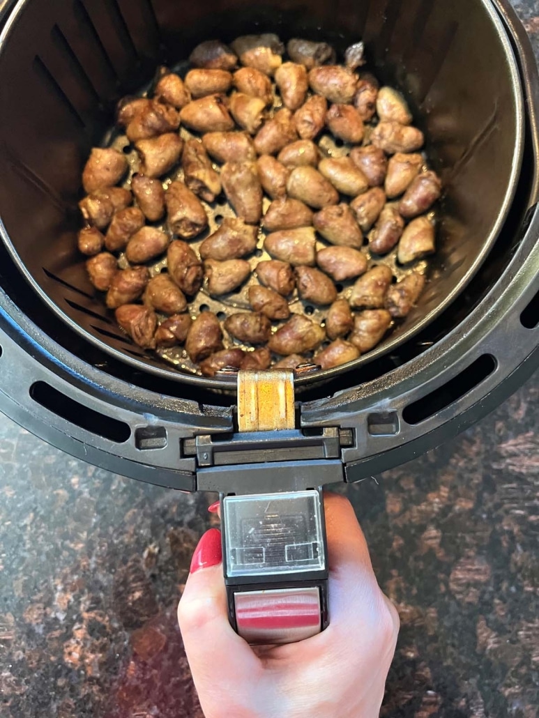 hand holding air fryer basket with delicious, golden brown chicken hearts inside