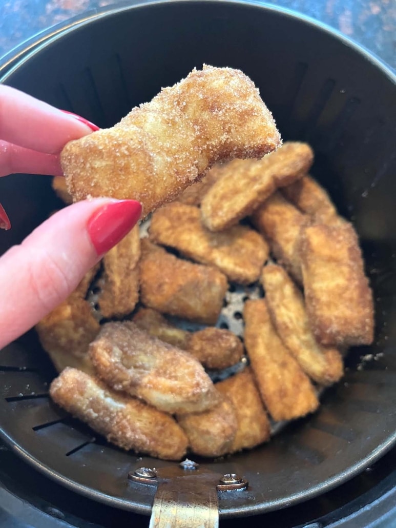 hand picking up churro from air fryer basket