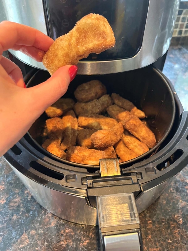 hand holding golden brown churro in front of open air fryer