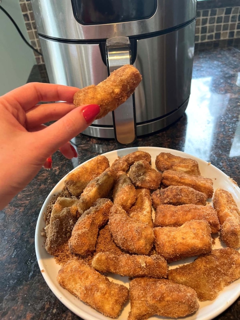 hand holding a churro in front of an air fryer