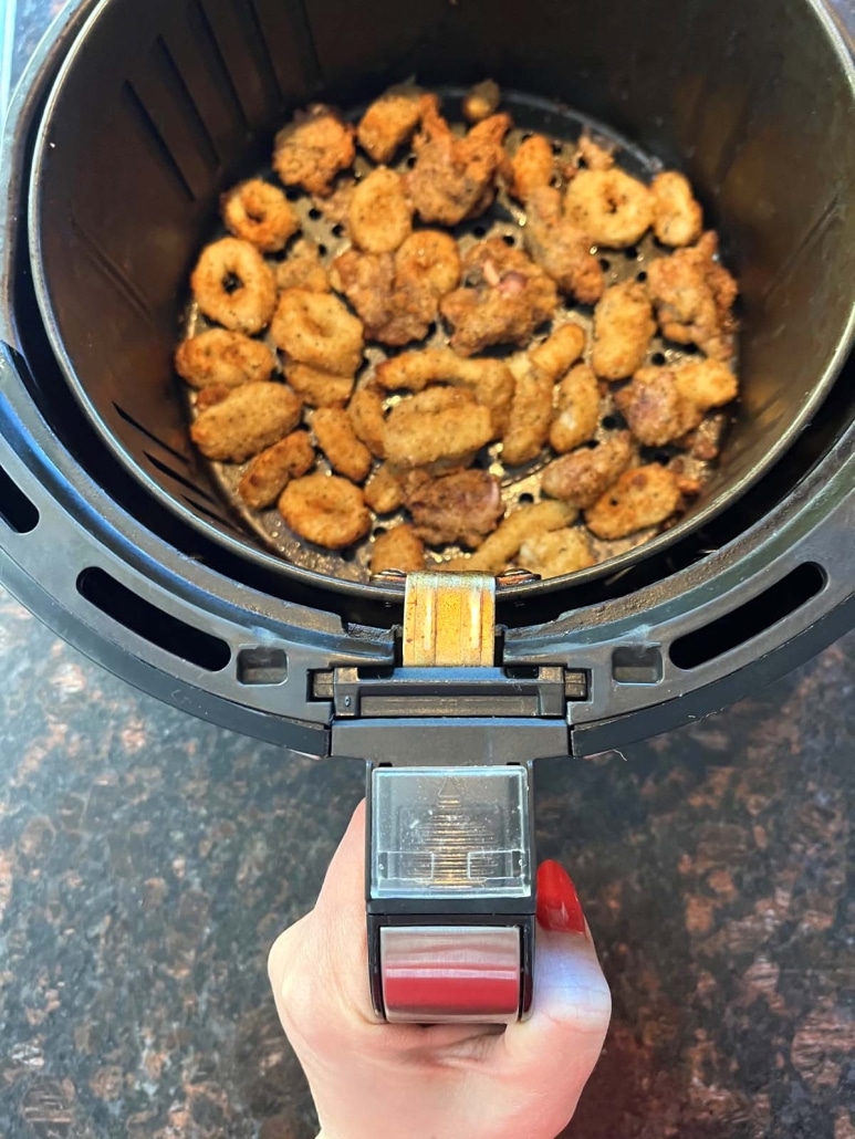 hand holding air fryer basket with breaded calamari inside