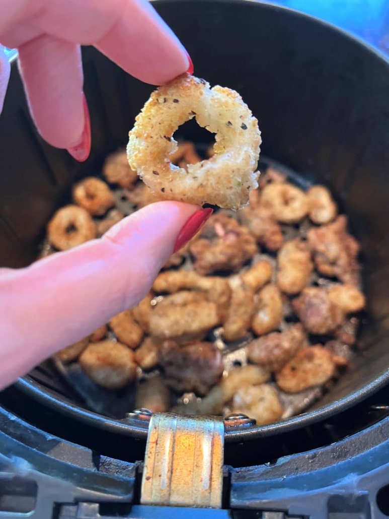 hand holding an air fried calamari ring above an air fryer basket