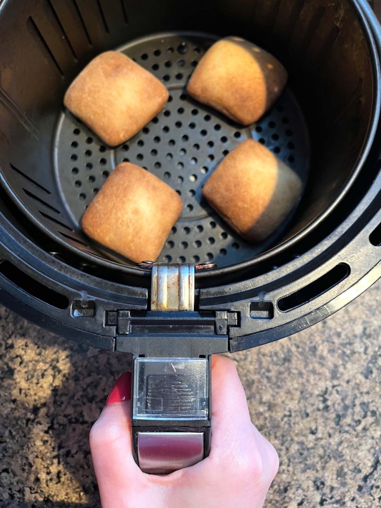 hand holding air fryer basket containing dinner rolls