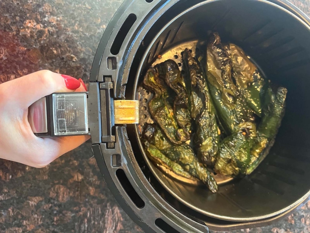 hand holding air fryer basket with cooked poblanos inside