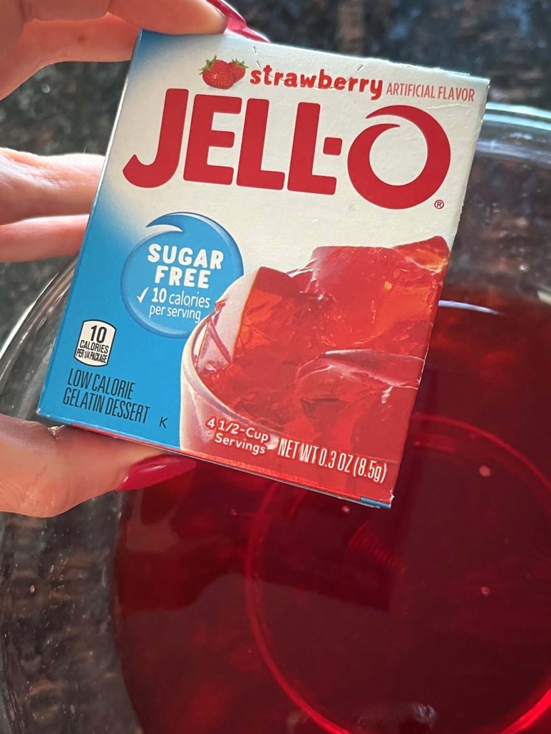 holding a box of Jello mix in front of a bowl of Jello