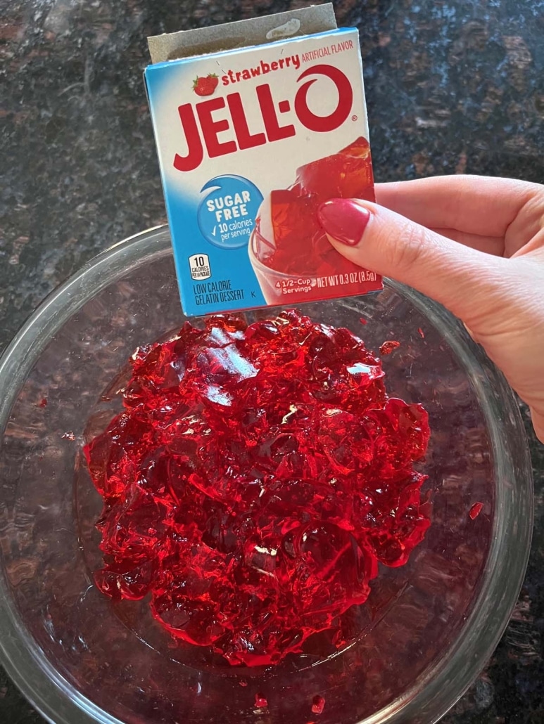 hand holding a box of Jello in front of a bowl of stirred Jello