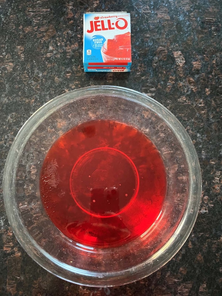 3 oz box of Jello mix next to a bowl of red Jello