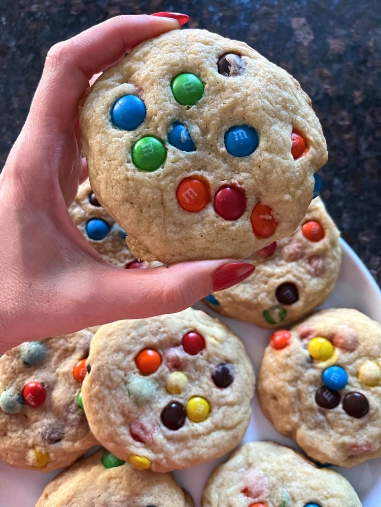 hand holding an M&M Cookie in front of a plate of cookies