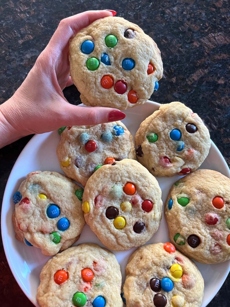 hand holding an M&M Cookie next to a plate of cookies