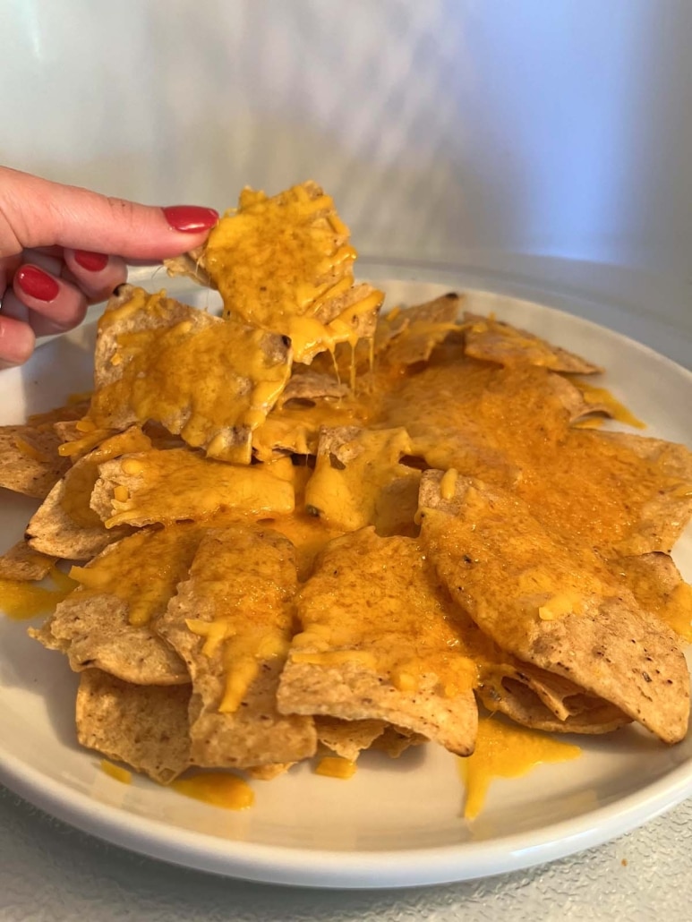 hand holding tortilla chip with melted cheese on it