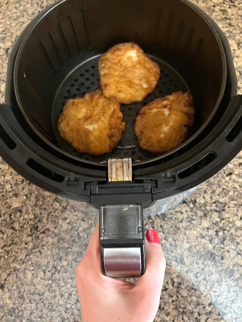 hand holding air fryer basket with breaded chicken fillets inside