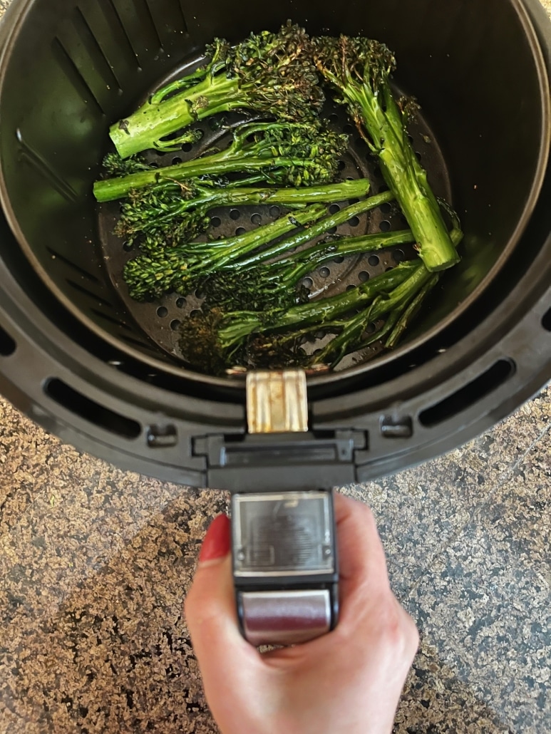 hand holding air fryer basket with cooked broccolini inside