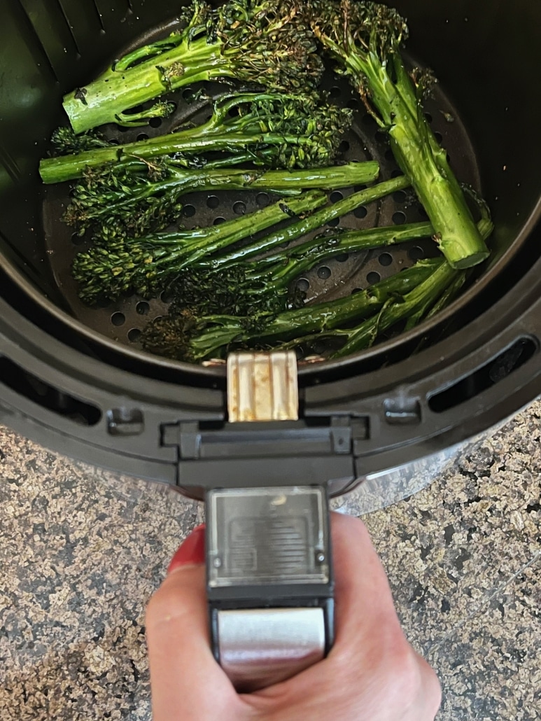 hand holding air fryer basket containing healthy side dish air fryer broccolini