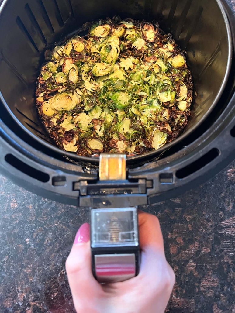 hand holding air fryer basket with cooked brussels sprouts inside